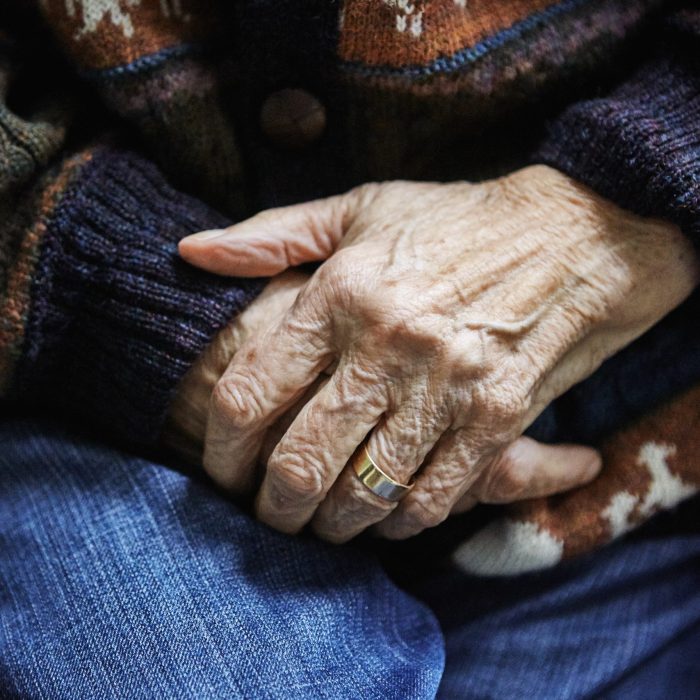 Senior woman sitting in chair, hands clasped, close-up